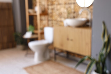 Modern toilet bowl, chest of drawers with sink and shelving unit near wooden wall in restroom. Blurred view