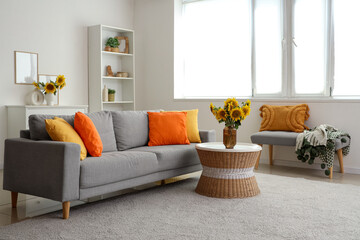 Stylish living room with grey sofa and vases of sunflowers bouquets on coffee table
