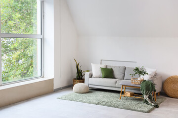 Interior of light living room with grey sofa, soft bench and poufs