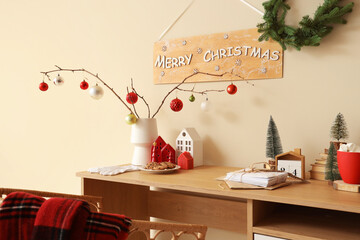 Vase with tree branches, Christmas balls and house candle holders on table in office