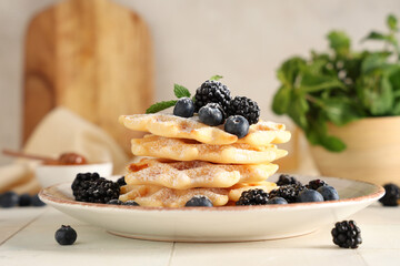 Delicious Belgian waffles with blueberries, blackberries and sugar powder on plate on table against white background