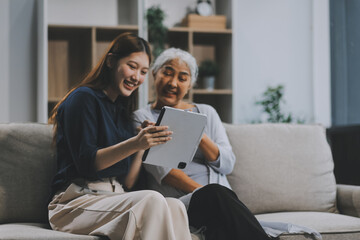 Happy grownup daughter showing content on tablet to mature mother. Two family generations women with digital computer gadget resting on couch together, watching videos, making video call