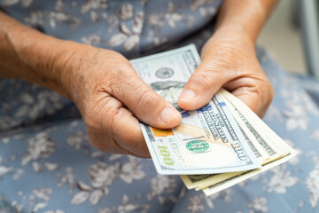 Asian senior woman holding and counting US dollar banknotes money in purse. Poverty, saving problem in retirement.