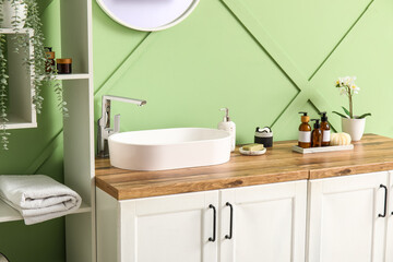 Chest of drawers with sink and bath supplies near green wall in bathroom