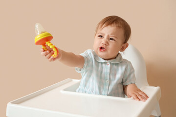 Crying little baby with nibbler in high chair on beige background