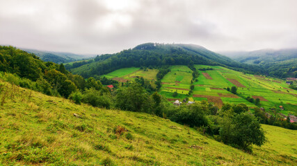 Fototapeta premium mountainous countryside landscape in autumn. grassy meadow on a hill. village in the distant valley. rural scenery. rainy weather with cloudy sky