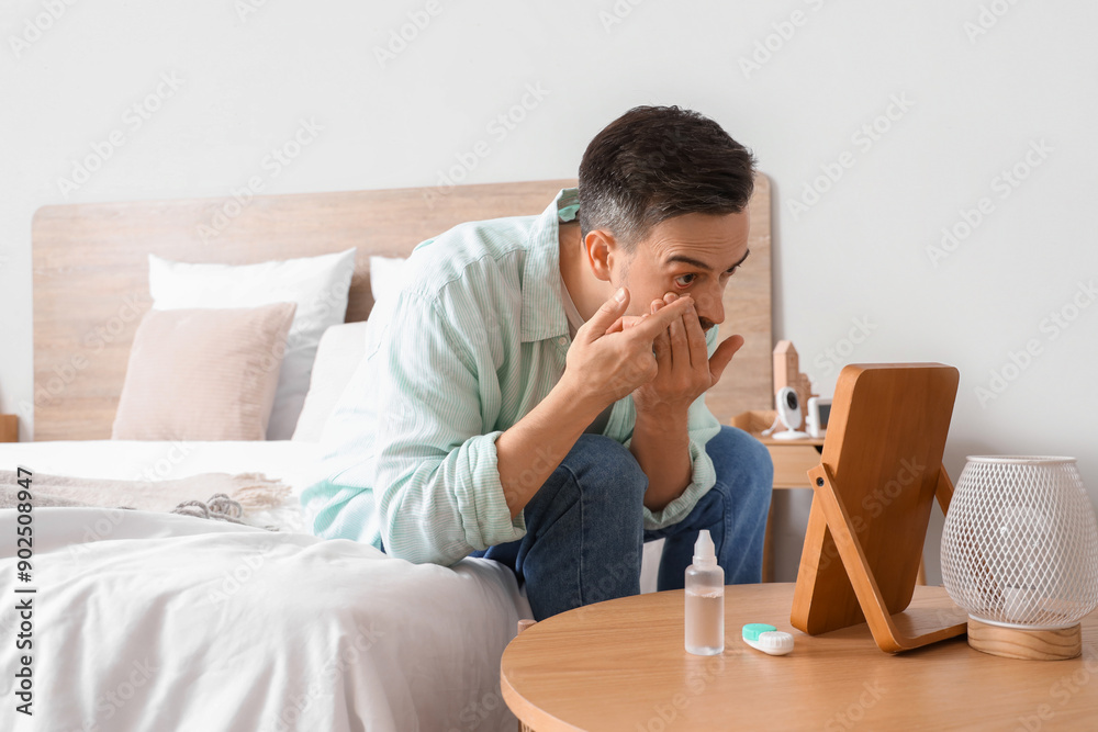 Wall mural young man with mirror putting in contact lenses at home