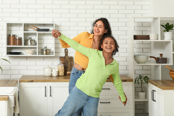 Beautiful young happy African-American mother with her daughter in kitchen at home