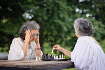 Two Elderly Women Engaged in a Strategic Chess Game Outdoors, Demonstrating Mental Sharpness and Social Bonding