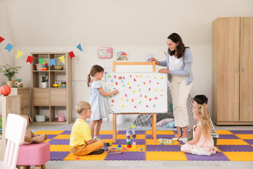 Little children with nursery teacher learning letters in kindergarten