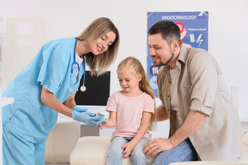 Fototapeta premium Female endocrinologist measuring blood sugar level of little girl and her father in clinic