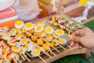 Fried Quail eggs in bamboo skewers on woman hand, serve warm with salt and ground pepper.