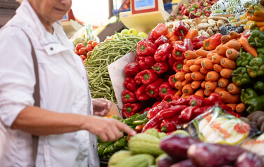 Senior woman buying fresh fruit and vegetables at the market, choosing from a large selection. Healthy eating, the concept of spending and consumerism