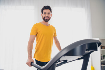 Photo of attractive cheerful strong man practicing physical exercises treadmill indoors home gym