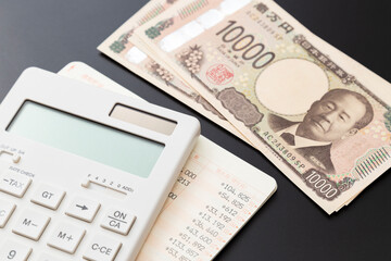 黒背景に電卓と預金通帳と一万円