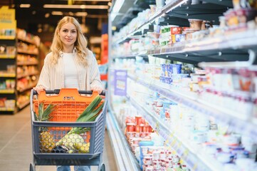 Young cool customer woman wear casual clothes shopping at supermaket store grocery shop buying with trolley cart choose products inside hypermarket