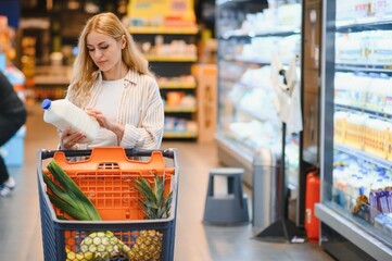 Young woman in casual clothes shopping at supermaket grocery store buy choose dairy produce take milk