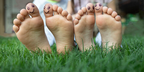 bare feet of two children sitting on grass with smiling faces painted on their big toes, close-up....