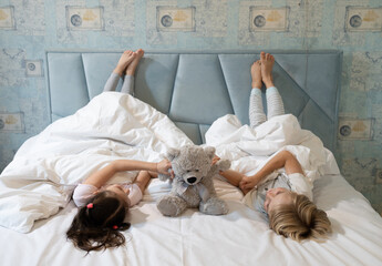 two children in pajamas, brother and sister, play with a toy teddy bear, lying upside down under a...