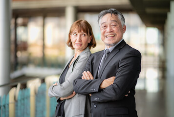 Portrait of mature Asian businessman and well-dressed Caucasian businesswoman standing in office working together. Two diverse colleagues, group of confident professional business people. Diversity.