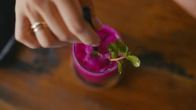 Top view of fresh exotic cocktail, woman stirring fruits and ice cubes in glass. Relax time in bar on beach, enjoying taste of cool fruity smoothie, travel in Thailand, tourism and gastronomy in Asia