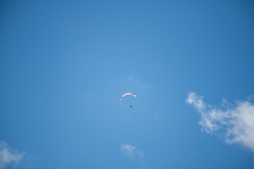 A solo paraglider soaring through a clear blue sky dotted with white clouds, capturing the essence...