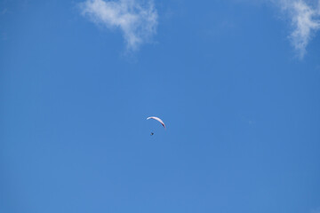 Solo paraglider flying high in a clear blue sky dotted with white clouds, epitomizing freedom and excitement