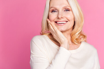 Photo of cheerful positive senior woman dressed stylish clothes touch face empty space isolated on pink color background