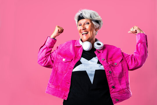 Beautiful senior woman with gray hair wearing colorful stylish clothing portrait in studio - Cheerful old grandmother with fashionable style flexing arm muscles