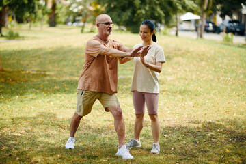 Senior Caucasian man engaging in outdoor exercise guided by young female instructor in park. Focus on fitness and healthy lifestyle without gym equipment present