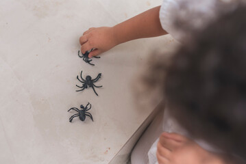A young asian boy plays with fake rubber toy spiders while sitting on the porch. He is fully engaged and focused on his playtime.