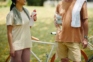 Two people standing outdoors engaging in conversation while holding water bottles after exercise....