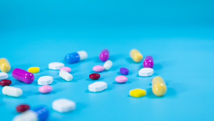 Multi-colored pills and capsules used in medical treatment are scattered on a blue background. Medicines used in medical treatment. Healthcare and medical concept. Space for text.