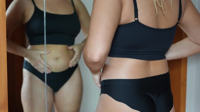 Fat deposits on the abdomen. A cropped shot of a young woman grabbing for belly fat standing in front of the mirror. Overeating, overweight, excess weight, hormonal changes
