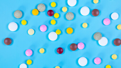 Multi-colored pills used in medical treatment are scattered on a blue background. Medicines used in medical treatment. Healthcare and medical concept. Space for text.