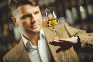 Sommelier holding a glass of whiskey, evaluates the color, smell and taste of alcoholic beverage.