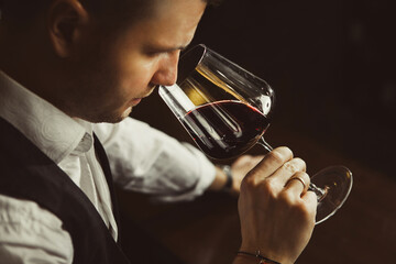 Close-up shot of young sommelier smell red wine on black background. © Ilshat
