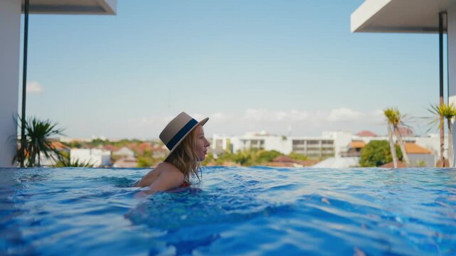 Woman swimming in beautiful endless pool in luxury apartment with city view. Attractive female tourist relaxing in resort hotel, slow motion, enjoy solitude in cool water, refreshing in hot summer day