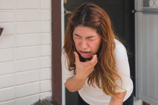 A asian woman in her 30s suddenly winces in pain from a bad toothache.