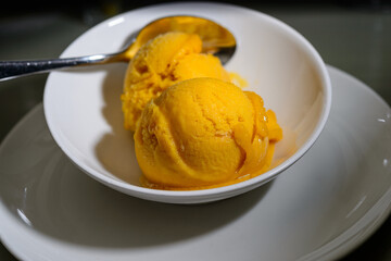 Two scoops of mango sorbet in a white bowl with a spoon.