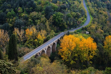 The picturesque authentic Italian landscape in Tuscany, Italy. Arched bridge and road in a autumn forest.
