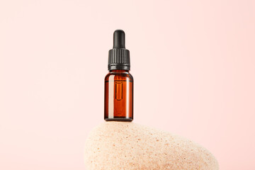 Glass amber vial on spa stone on pink background.