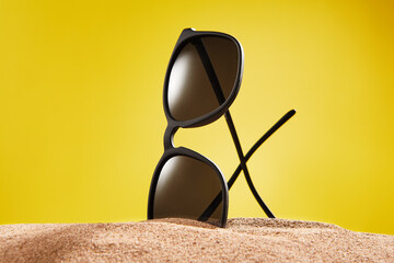 Rimmed sun glasses is on sand on yellow background.