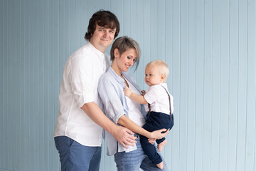 Happy family mother and father with baby toddler son on hands, near a blue wooden wall and smiling at home, happy family