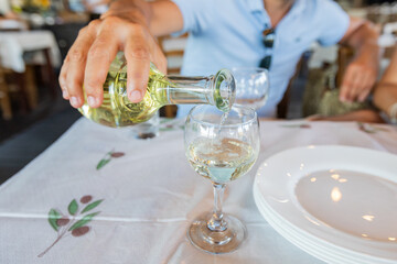 Man pours wine into a glass in a traditional greek restaurant.