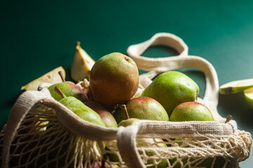 Ripe pears in a string bag on a green background