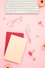 Office chic stylish workspace with keyboard, glasses and stationery on pink background. Perfect for modern professionals
