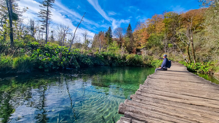 Hiker man sitting on enchanting hiking trail on rustical wooden footpath in Plitvice lakes National Park, Karlovac, Croatia, Europe. Bridge over turquoise water in idyllic paradise nature. Wanderlust