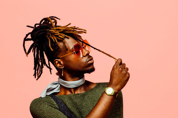 Portrait of a young man in green with dreadlocks and blue sunglasses, isolated on pink