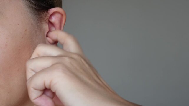 Young caucasian woman scratching her ear with the finger on a dark gray background. Fungal infection, allergy, eczema, psoriasis, candidiasis, otomycosis, itch, itching, peeling, dermatitis